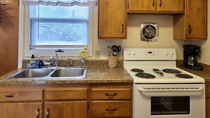A kitchen with wooden cabinets, a double sink, a stove, and a window with blinds.