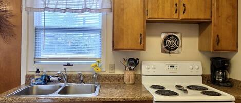 A kitchen with wooden cabinets, a double sink, a stove, and a window with blinds.