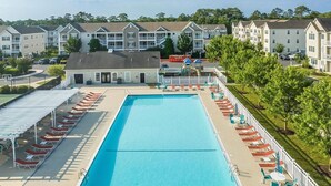 Une piscine entourée de bâtiments à plusieurs étages dotés de balcons, avec des chaises longues et des parasols à proximité.