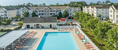 A swimming pool with lounge chairs and umbrellas, surrounded by multi-story buildings with balconies.