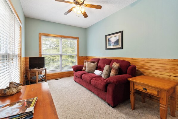 A cozy living room with a red sofa, wooden side table, and a ceiling fan.