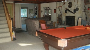 A cozy living room with a pool table, a fireplace, and a staircase leading to another room. - Caron Hideaway - Lakefront House - Private Pool and Beach (Willsboro)
