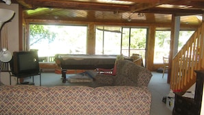 A cozy living room with a patterned sofa, a television, and a large window offering a view of the outdoors. - Caron Hideaway - Lakefront House - Private Pool and Beach (Willsboro)