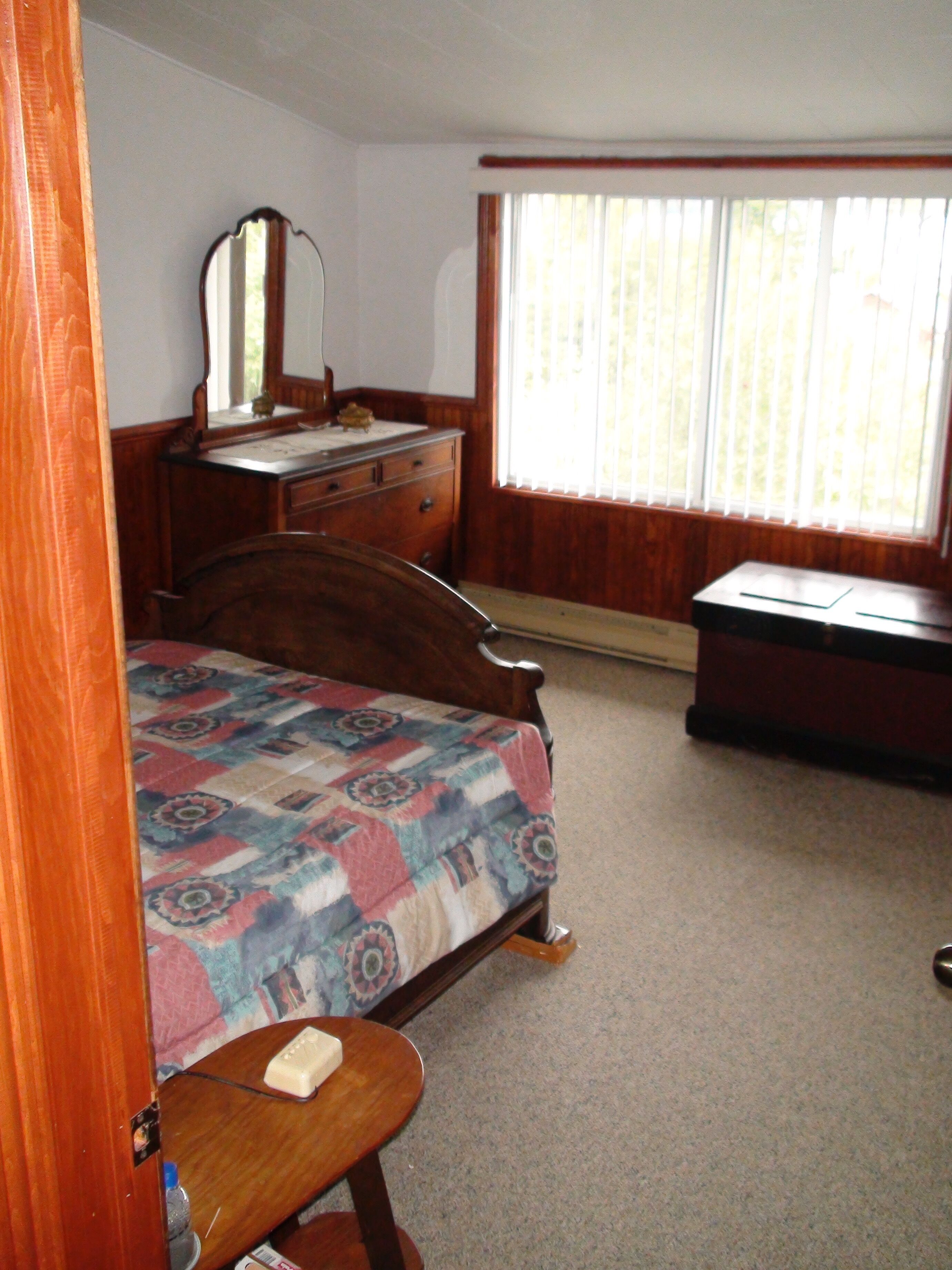 Une chambre à coucher avec un lit, une commode et une fenêtre équipée de stores.