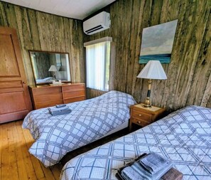 Una habitación con dos camas, paredes de madera, un espejo, un aparador y un aire acondicionado.