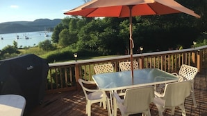 A deck with a glass table and white chairs, overlooking a lake with boats. - Caron Hideaway - Lakefront House - Private Pool and Beach (Willsboro)