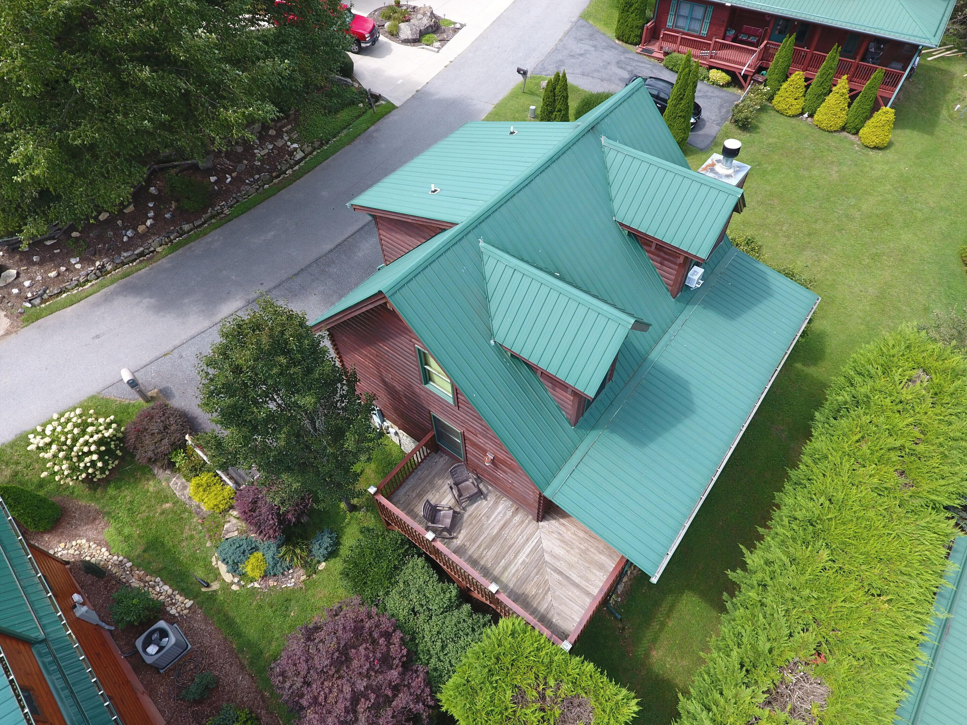 A two-story house with a green roof, a wooden deck, and a landscaped garden.