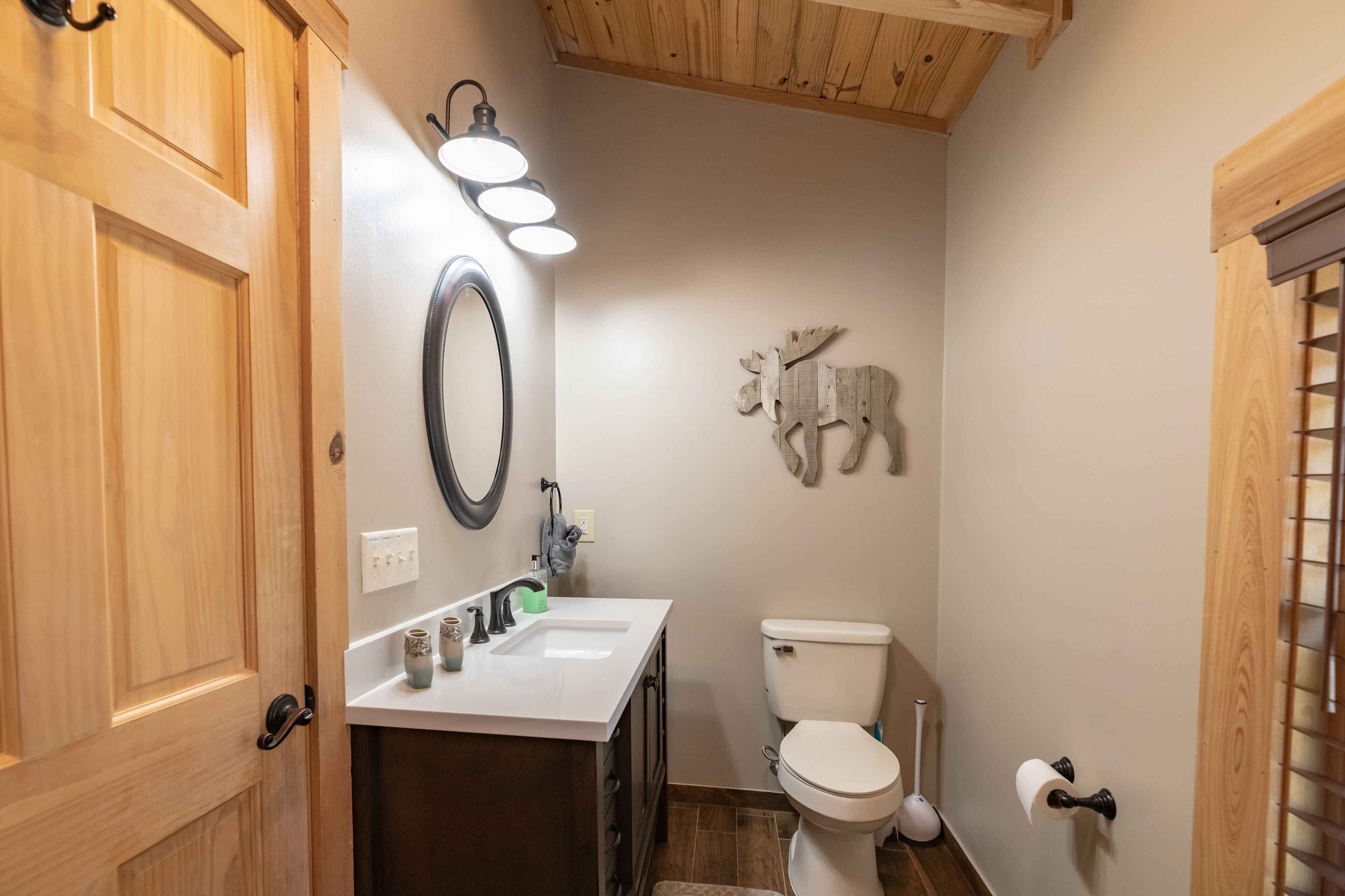 A bathroom with a wooden door, a white sink with a mirror, a toilet, and a wall-mounted light fixture.