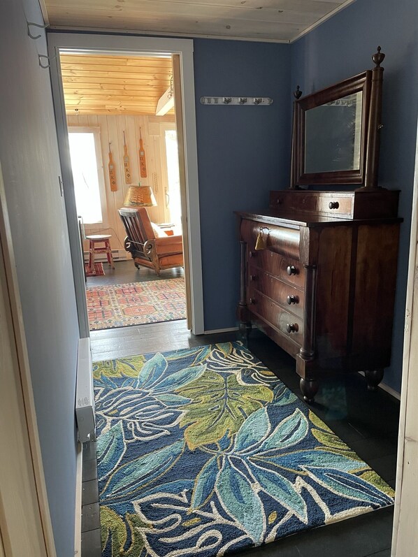 A room with a wooden floor, a patterned rug, a dresser, and a mirror.