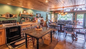 A rustic kitchen with wooden cabinets, a black stove, and a dining area with wooden chairs and a table. - ~ Lakeside Log Cabin ~ Blessings & Memories Abound! (Graham)