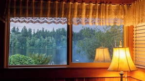 A room with a window overlooking a lake and forest, a lamp on the right, and a wooden wall. - ~ Lakeside Log Cabin ~ Blessings & Memories Abound! (Graham)