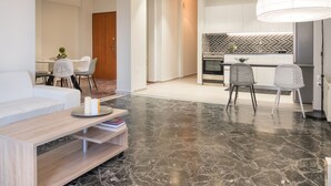 Een moderne woonkamer met een bank, salontafel en stoelen. Er is een keukenhoek met een eettafel en stoelen.