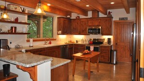 A kitchen with wooden cabinets, a granite countertop, a stainless steel sink, and a window with a view of trees. - Private Riverfront Lodge with Mountain Views Between Lost Maples and Garner Park (Vanderpool)