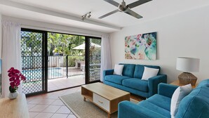 Una sala de estar con un sofá azul, una mesa de centro, un cuadro y un ventilador de techo.