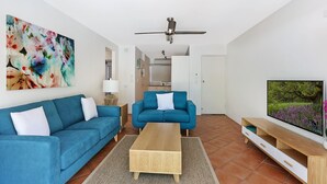 Una sala de estar moderna con un sofá azul, una mesa de centro de madera y un televisor sobre un mueble de madera.