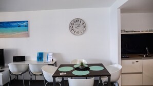 Une cuisine moderne avec des meubles blancs, un évier et un coin repas comprenant une table et des chaises. Une horloge est fixée au mur au-dessus du coin repas.