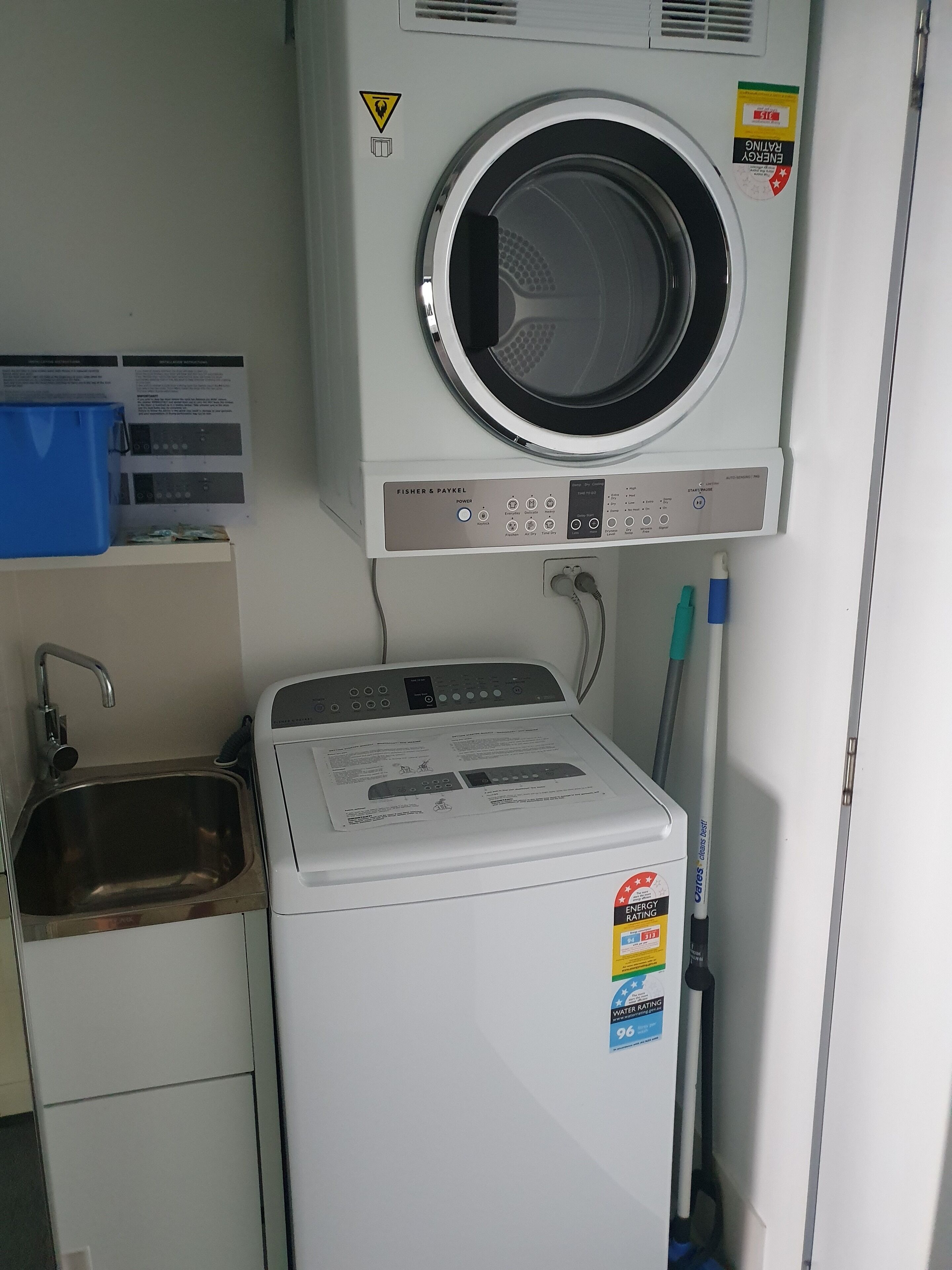 Un espace buanderie comprenant un lave-linge et un sèche-linge à chargement frontal, un évier et un bac de rangement bleu.