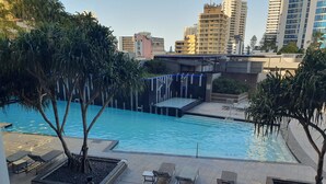 Une piscine entourée d’arbres et de bâtiments, avec des chaises longues et une scène.