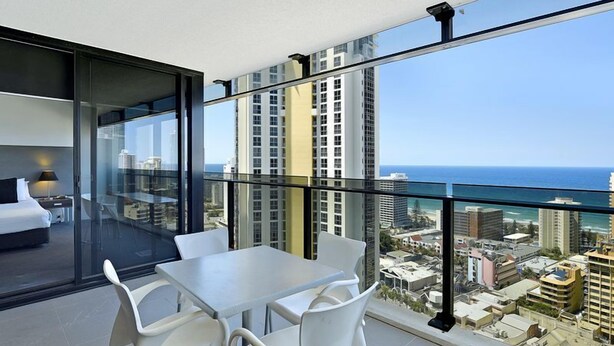 Un balcon moderne avec une paroi en verre, des meubles blancs et une vue sur la ville, qui s’étend jusqu’à l’océan.