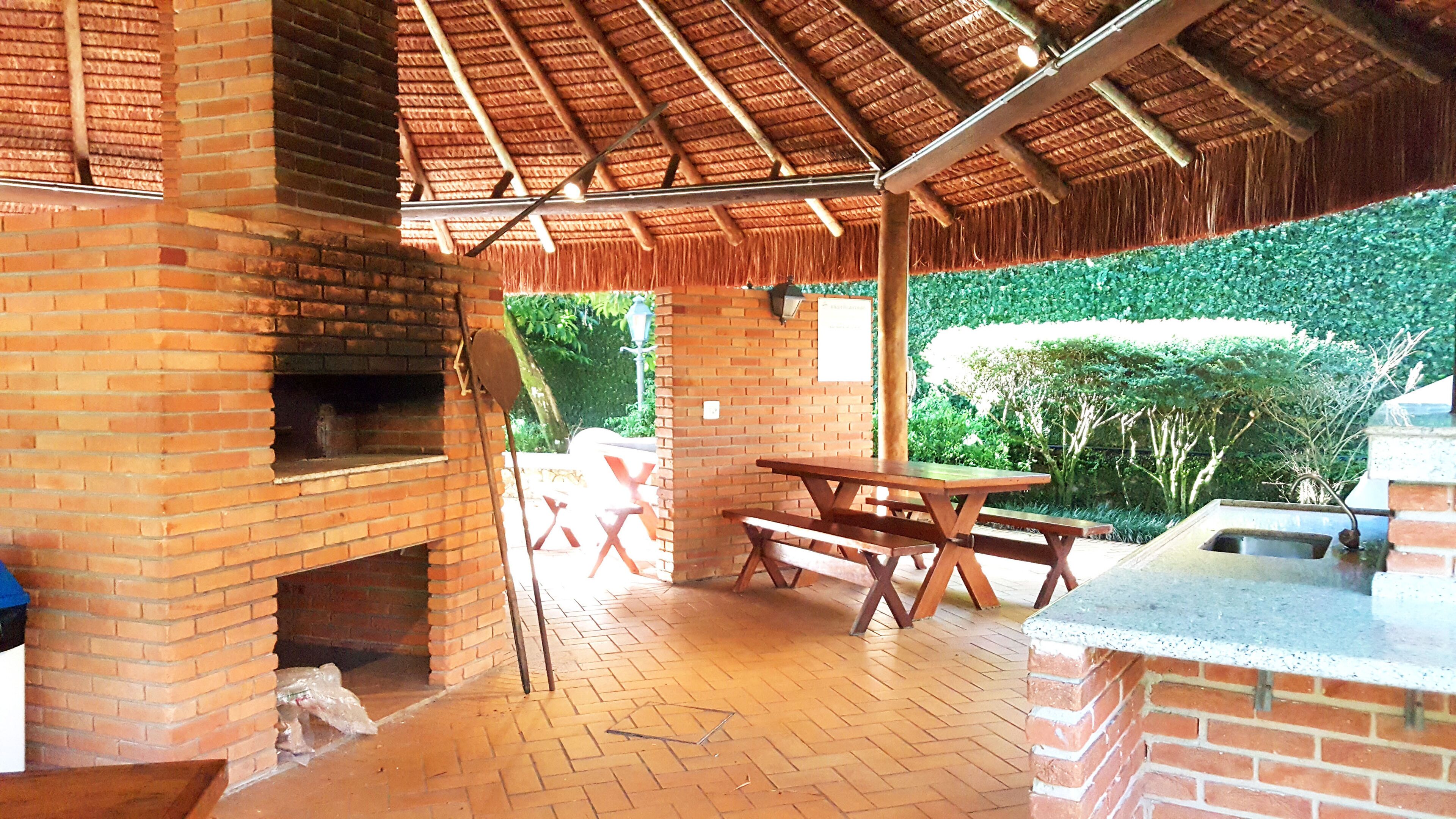 Eine Terrasse im Freien mit Kamin aus Ziegelsteinen, einem Holztisch und einem Grill.