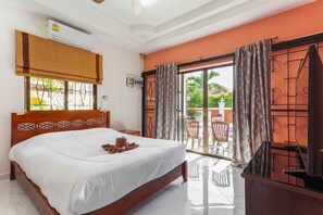 A hotel room with a wooden bed, an air conditioning unit, a balcony with a view of greenery, and a sliding glass door.