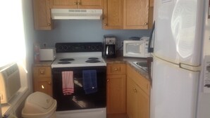 A compact kitchen with wooden cabinets, a stove, a microwave, and a refrigerator. - Carry Bay Cozy Cottage-Lake Champlain Cabin 4 (North Hero)