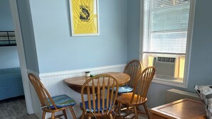 A dining area with a wooden table and chairs, a framed picture on the wall, and a window with blinds. - Carry Bay Cozy Cottage-Lake Champlain Cabin 4 (North Hero)