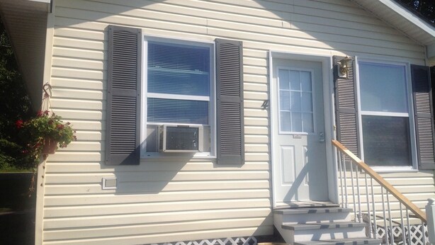 A house with a front porch, two windows with shutters, a door, and a staircase leading to the entrance. - Carry Bay Cozy Cottage-Lake Champlain Cabin 4 (North Hero)