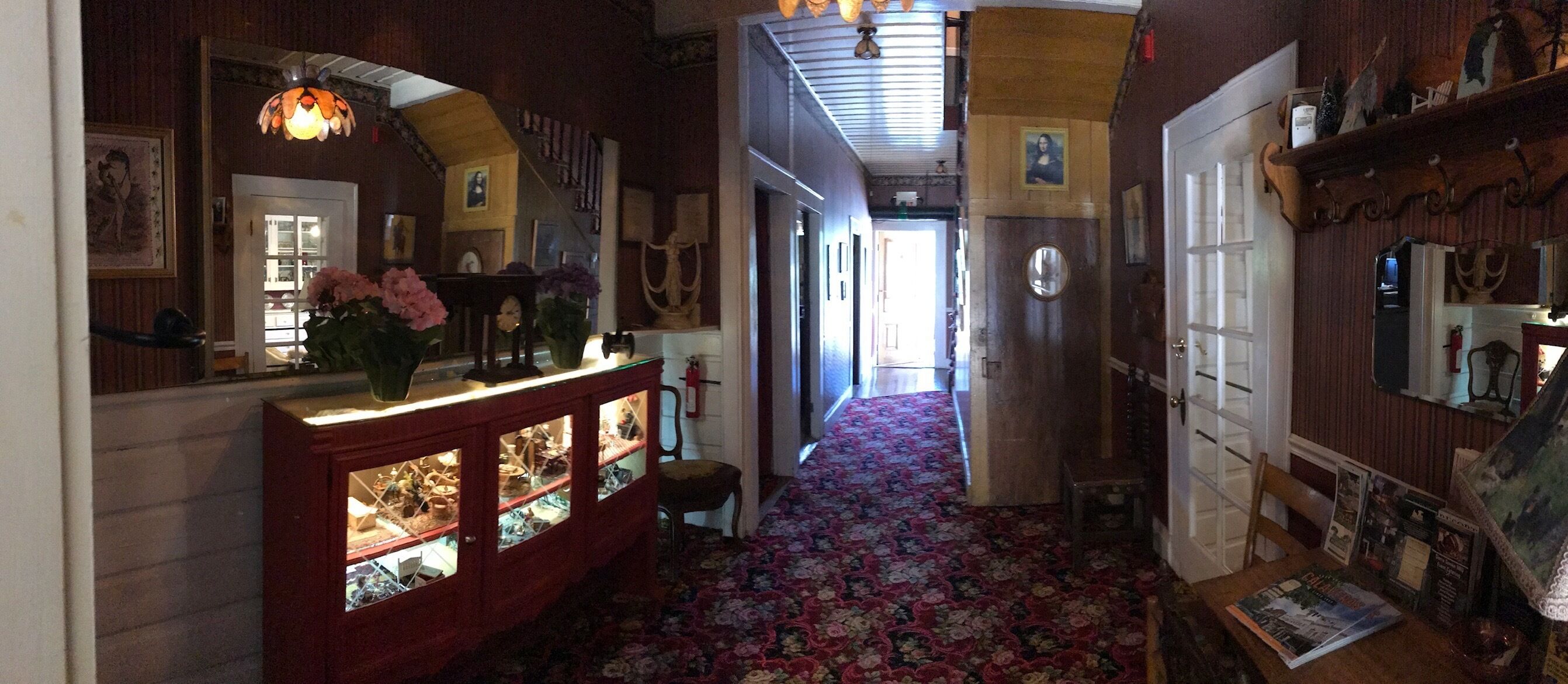 A hallway with a floral carpet, wooden cabinets with glass doors, and a staircase with a wooden railing.