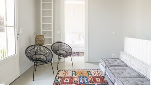 Ett rum med en vit soffa, två svarta stolar med stomme av metalltråd, en färgglad matta och en vit stege som leder upp till ett loft.