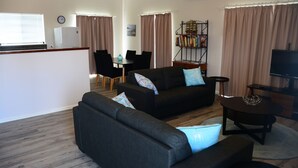 A modern living room with a sofa set, a dining area, and a TV.