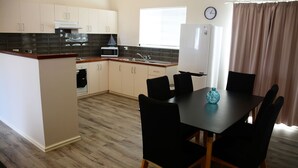 A compact kitchen with a dining area, featuring a microwave, oven, and a clock on the wall.