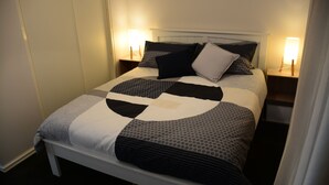 A neatly made bed with a geometric patterned bedspread, two bedside lamps, and a white headboard.