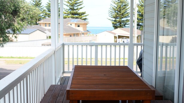 A wooden bench on a covered porch with a view of houses and the sea.