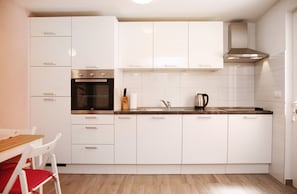Uma cozinha moderna com armários brancos, forno embutido e exaustor de aço inoxidável.