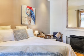 A hotel room with a large bed, a painting on the wall, a fireplace, and a mirror.