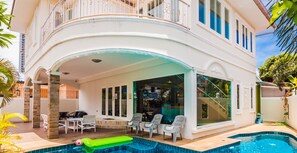A two-story building with a covered patio area featuring a pool, outdoor seating, and a staircase leading to an upper balcony.