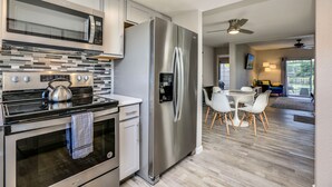 Een moderne keuken met roestvrijstalen apparatuur, een eethoek met witte stoelen en uitzicht op de achtertuin.