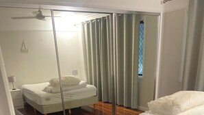Quarto com cama, um banquinho, espelho e ventilador de teto.