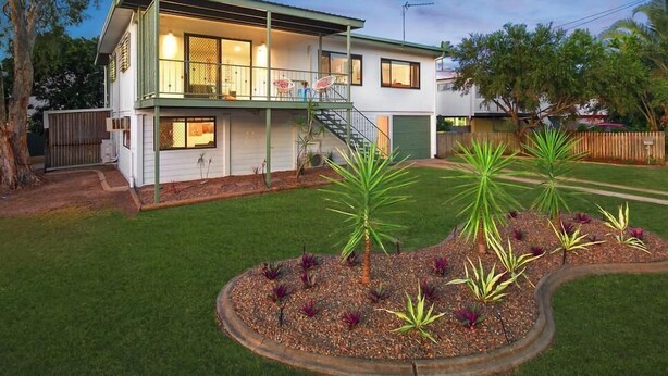 Uma casa de dois andares com uma varanda, escadas e um gramado bem cuidado, com plantas.