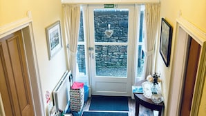 A hallway with a chandelier, a fire exit sign, a stone wall, and a door with a doormat. - Heritage house in great location under Stirling castle, close to amenities. (Stirling)