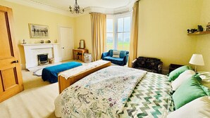 A bedroom with a bed, two chairs, a dresser, a mirror, a fireplace, and a window with curtains. - Heritage house in great location under Stirling castle, close to amenities. (Stirling)