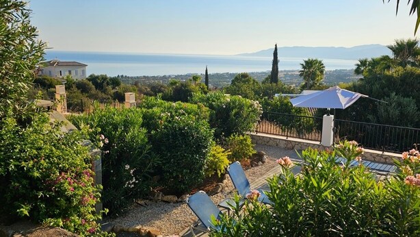 Ein Garten mit Blick auf das Meer, ein weißes Gebäude und eine Steinsäule.