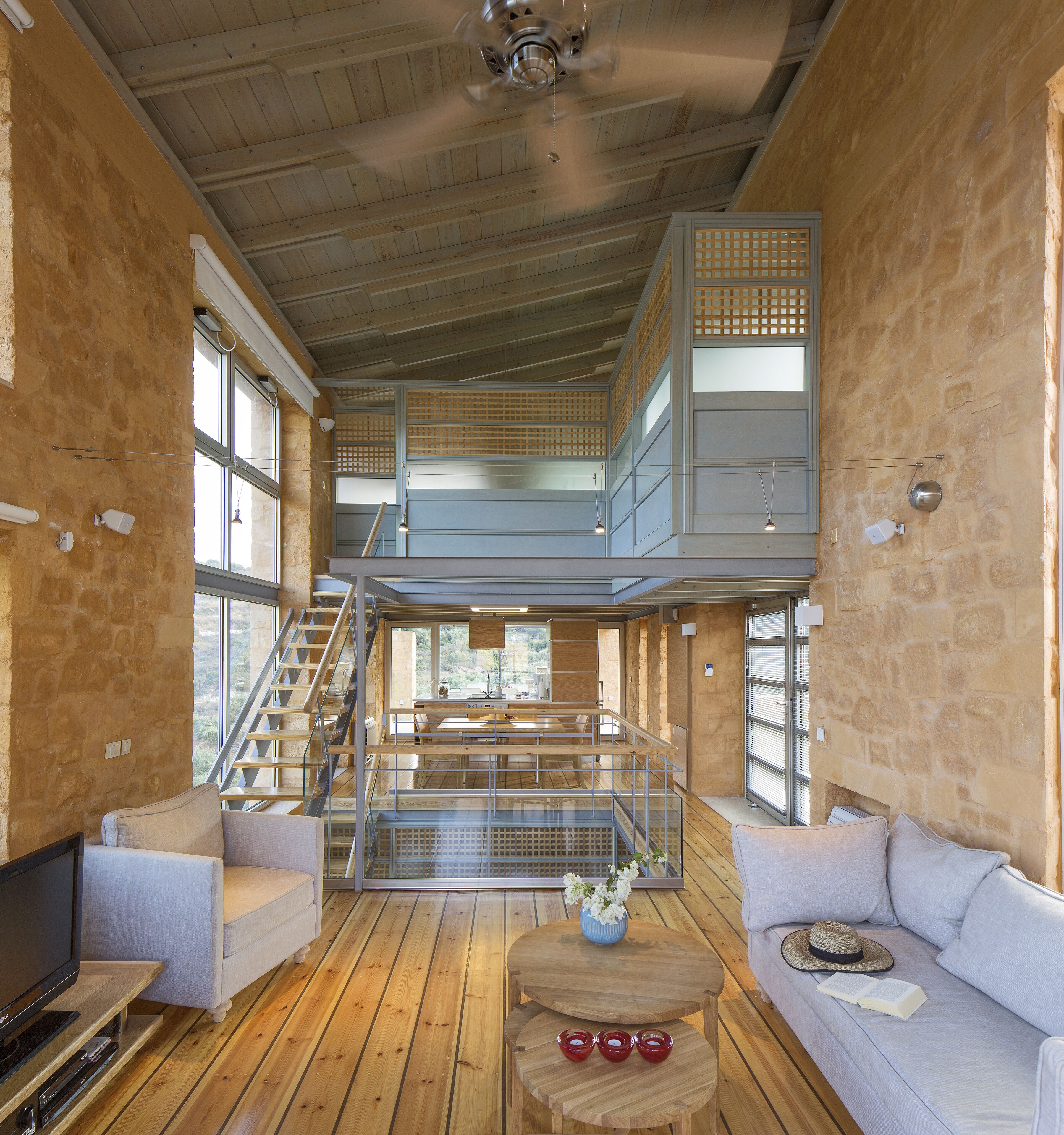 Un intérieur spacieux avec un plafond haut, des planchers en bois, un escalier menant à un niveau supérieur et un coin salon équipé d’un téléviseur.