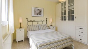 A bedroom with a bed, two bedside tables with lamps, a framed picture on the wall, and a wardrobe with drawers.
