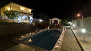 A swimming pool with a tiled deck, a covered patio area, and a building with a balcony.