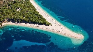 An aerial view of a coastal area with a long sandy beach, clear blue waters, and dense green vegetation. - House with a unique view of the sea, islands in a quite position, EV-ready (Kaštel Sućurac)
