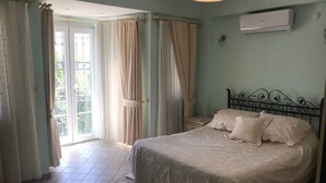 Un dormitorio con cama, cortinas, un equipo de aire acondicionado y vista a través de una puerta.