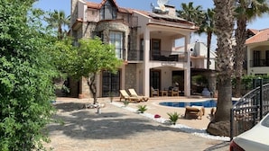 Una casa grande de varios pisos con piscina, mobiliario exterior y palmeras.