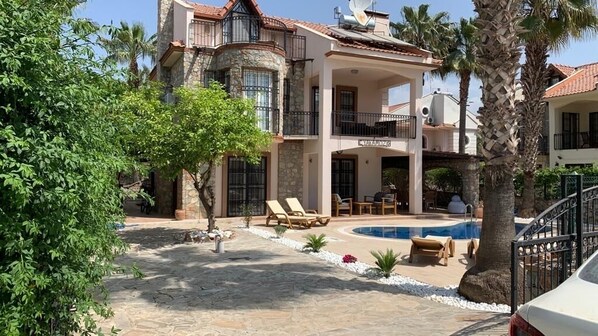 A large, multi-story house with a swimming pool, outdoor seating, and palm trees.